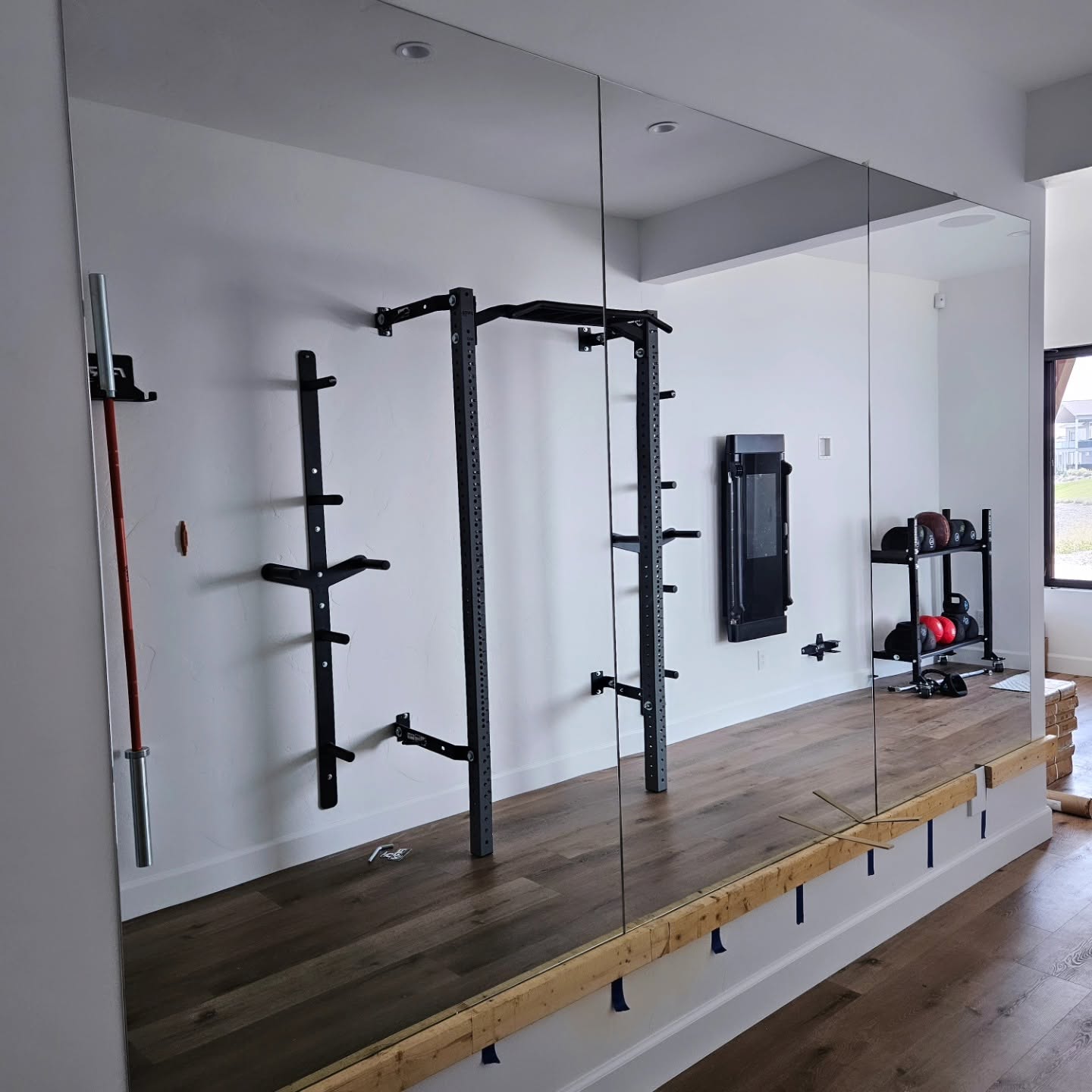 Full mirror wall reflecting a wall-mounted squat rack in a Chelan WA home gym