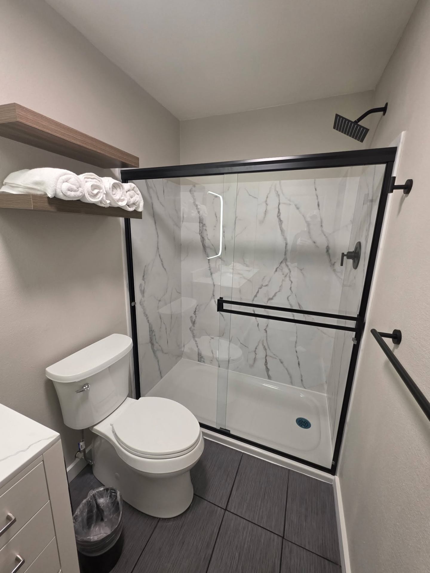 Bathroom remodel showing shower, toilet, and floating wood shelf